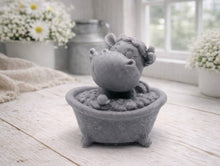 Load image into Gallery viewer, A handmade vegan soap is sculpted in the shape of a "dirty cow" character happily sitting in a bubble-filled roll-top bathtub with one hoof raised, displayed on a light wooden surface.