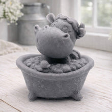Load image into Gallery viewer, A handmade vegan soap is sculpted in the shape of a "dirty cow" character happily sitting in a bubble-filled roll-top bathtub with one hoof raised, displayed on a light wooden surface.