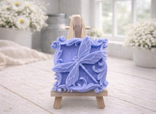 Load image into Gallery viewer, A beautiful handmade vegan soap in a natural tone, featuring a highly detailed relief of a dragonfly with delicate, outspread wings and a textured body, displayed on a miniature wooden easel against a soft farmhouse background.
