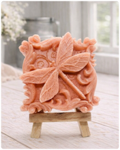 Load image into Gallery viewer, A beautiful handmade vegan soap in a natural tone, featuring a highly detailed relief of a dragonfly with delicate, outspread wings and a textured body, displayed on a miniature wooden easel against a soft farmhouse background.