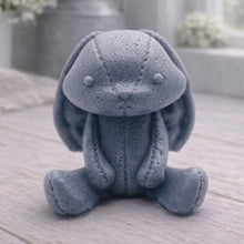Load image into Gallery viewer, A handmade vegan soap sculpted in the shape of a sitting floppy-eared bunny rabbit with visible stitched seam details like a plush toy, in a soft grey tone, displayed on a light wooden surface.