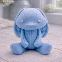 Load image into Gallery viewer, A handmade vegan soap sculpted in the shape of a sitting floppy-eared bunny rabbit with visible stitched seam details like a plush toy, in a soft blue tone, displayed on a light wooden surface.