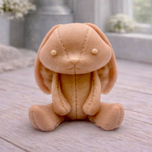 Load image into Gallery viewer, A handmade vegan soap sculpted in the shape of a sitting floppy-eared bunny rabbit with visible stitched seam details like a plush toy, in a soft peach-orange tone, displayed on a light wooden surface.