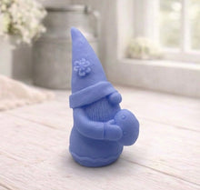 Load image into Gallery viewer, handmade vegan soap in the shape of a sitting gnome holding a decorated Easter egg, featuring a tall pointed hat with a flower detail and a textured beard, displayed on a neutral cloth in a bright spring setting.