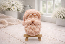 Load image into Gallery viewer, handmade vegan soap sculpted in the shape of Father Christmas's head, featuring a detailed curly beard, a jolly moustache, and a classic Santa hat, displayed on a miniature wooden easel in a bright farmhouse setting.