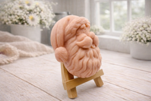 Load image into Gallery viewer, handmade vegan soap sculpted in the shape of Father Christmas's head, featuring a detailed curly beard, a jolly moustache, and a classic Santa hat, displayed on a miniature wooden easel in a bright farmhouse setting.