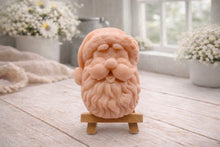 Load image into Gallery viewer, handmade vegan soap sculpted in the shape of Father Christmas's head, featuring a detailed curly beard, a jolly moustache, and a classic Santa hat, displayed on a miniature wooden easel in a bright farmhouse setting.