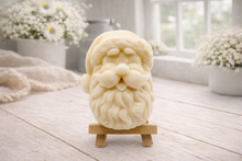 Load image into Gallery viewer, handmade vegan soap sculpted in the shape of Father Christmas's head, featuring a detailed curly beard, a jolly moustache, and a classic Santa hat, displayed on a miniature wooden easel in a bright farmhouse setting.
