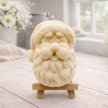 Load image into Gallery viewer, handmade vegan soap sculpted in the shape of Father Christmas's head, featuring a detailed curly beard, a jolly moustache, and a classic Santa hat, displayed on a miniature wooden easel in a bright farmhouse setting.