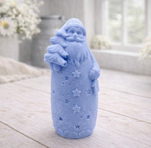 Load image into Gallery viewer, handmade vegan soap sculpted into a tall figure of Father Christmas wearing star-patterned robes, holding a small Christmas tree in one arm and a lantern in the other, set in a bright farmhouse window.