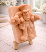 Load image into Gallery viewer, A rectangular handmade vegan soap featuring a high-relief carving of Frankenstein's monster in a classic pose with arms outstretched and a grumpy expression, displayed on a miniature wooden easel.