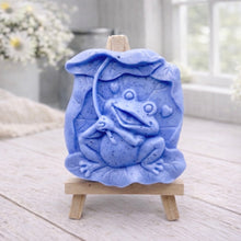Load image into Gallery viewer, A rectangular handmade vegan soap featuring a high-relief carving of a cheerful, smiling frog sitting on a large lilypad and holding the stem of a leaf over its head like an umbrella.