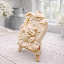 Load image into Gallery viewer, A rectangular handmade vegan soap featuring a high-relief carving of a cheerful, smiling frog sitting on a large lilypad and holding the stem of a leaf over its head like an umbrella.