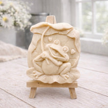 Load image into Gallery viewer, A rectangular handmade vegan soap featuring a high-relief carving of a cheerful, smiling frog sitting on a large lilypad and holding the stem of a leaf over its head like an umbrella.