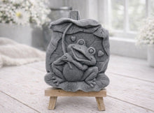 Load image into Gallery viewer, A rectangular handmade vegan soap featuring a high-relief carving of a cheerful, smiling frog sitting on a large lilypad and holding the stem of a leaf over its head like an umbrella.