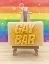 Load image into Gallery viewer, Bar of soap with 'GAY BAR' text on a wooden stand against a rainbow background