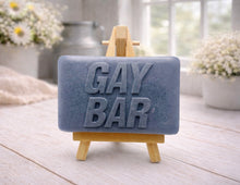 Load image into Gallery viewer, A rectangular handmade vegan soap featuring the words "GAY BAR" in large, bold, 3D block lettering, displayed on a miniature wooden easel.