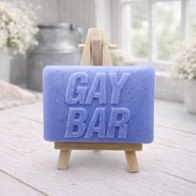 Load image into Gallery viewer, A rectangular handmade vegan soap featuring the words "GAY BAR" in large, bold, 3D block lettering, displayed on a miniature wooden easel.