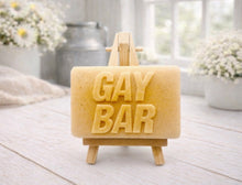 Load image into Gallery viewer, A rectangular handmade vegan soap featuring the words "GAY BAR" in large, bold, 3D block lettering, displayed on a miniature wooden easel.