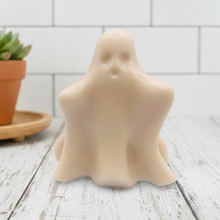 Load image into Gallery viewer, A handmade vegan soap shaped like a friendly ghost with a surprised expression, sitting on a light wood surface with white daisies in the background