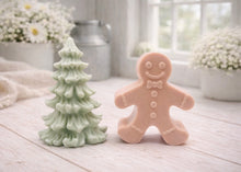 Load image into Gallery viewer, A handmade vegan soap featuring a classic gingerbread man with a smiling face, a bow tie, and decorative icing details on his arms and legs, and a Christmas tree - displayed on a miniature wooden easel.