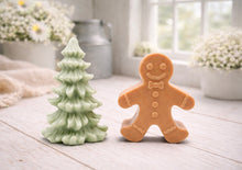 Load image into Gallery viewer, A handmade vegan soap featuring a classic gingerbread man with a smiling face, a bow tie, and decorative icing details on his arms and legs, and a Christmas tree - displayed on a miniature wooden easel.