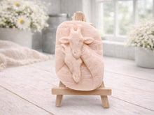 Load image into Gallery viewer, A rectangular handmade vegan soap in a natural tone, featuring a detailed relief of a mother and baby giraffe with their necks intertwined, displayed on a miniature wooden easel against a white wood-panelled background.