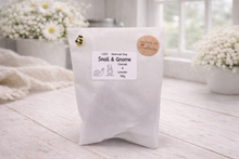 Load image into Gallery viewer, White packaging with a label on a light wooden surface, surrounded by white flowers.