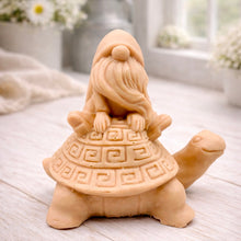 Load image into Gallery viewer, A handmade vegan soap in a natural tone, sculpted as a whimsical gnome (gonk) with a long beard sitting on the back of a large, smiling turtle with a patterned geometric shell.