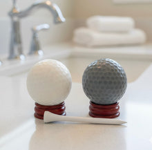 Load image into Gallery viewer, A set of two handmade vegan golf ball soaps in white and grey, displayed on miniature wooden stands with a golf tee in a bright farmhouse decor bathroom.