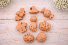 Load image into Gallery viewer, A collection of eight handmade vegan Halloween soaps featuring a bat, witch's hat, star-patterned sweet, haunted house, black cat, jack-o'-lantern, and a ghost, arranged on a light wooden surface with white floral accents.
