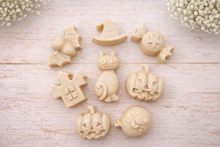 Load image into Gallery viewer, A collection of eight handmade vegan Halloween soaps featuring a bat, witch's hat, star-patterned sweet, haunted house, black cat, jack-o'-lantern, and a ghost, arranged on a light wooden surface with white floral accents.
