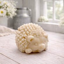 Load image into Gallery viewer, A detailed handmade vegan soap sculpted in the shape of a round, sitting hedgehog with intricate quill textures and a cute face, in a natural honey-brown tone, displayed on a light wooden surface.
