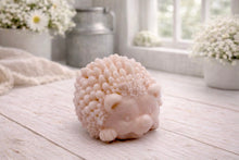 Load image into Gallery viewer, A detailed handmade vegan soap sculpted in the shape of a round, sitting hedgehog with intricate quill textures and a cute face, in a natural tone, displayed on a light wooden surface.