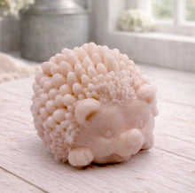 Load image into Gallery viewer, A detailed handmade vegan soap sculpted in the shape of a round, sitting hedgehog with intricate quill textures and a cute face, in a natural tone, displayed on a light wooden surface.