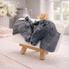 Load image into Gallery viewer, A rectangular handmade vegan soap featuring a detailed 3D relief of two horse heads leaning affectionately towards each other, finished in a slate-grey tone against a white soap base and displayed on a miniature wooden easel.