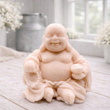 Load image into Gallery viewer, A 3D handmade vegan soap sculpted into a joyful Laughing Buddha sitting in a meditative pose, holding prayer beads and a small bowl, displayed in a bright farmhouse setting