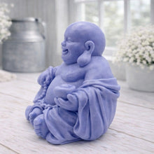 Load image into Gallery viewer, A 3D handmade vegan soap sculpted into a joyful Laughing Buddha sitting in a meditative pose, holding prayer beads and a small bowl, displayed in a bright farmhouse setting