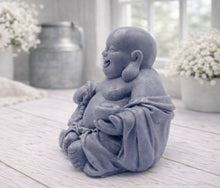 Load image into Gallery viewer, A 3D handmade vegan soap sculpted into a joyful Laughing Buddha sitting in a meditative pose, holding prayer beads and a small bowl, displayed in a bright farmhouse setting