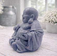 Load image into Gallery viewer, A 3D handmade vegan soap sculpted into a joyful Laughing Buddha sitting in a meditative pose, holding prayer beads and a small bowl, displayed in a bright farmhouse setting