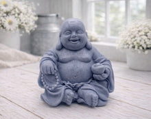 Load image into Gallery viewer, A 3D handmade vegan soap sculpted into a joyful Laughing Buddha sitting in a meditative pose, holding prayer beads and a small bowl, displayed in a bright farmhouse setting