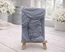 Load image into Gallery viewer, A rectangular handmade vegan soap featuring a high-relief carving of a mother tenderly cradling a small baby in her arms, displayed on a miniature wooden easel in a bright farmhouse setting.