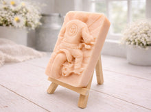 Load image into Gallery viewer, detailed handmade vegan soap gift featuring a motorcycle rider with a skull emblem on their jacket, displayed on a wooden easel against a whimsical farmhouse decor background