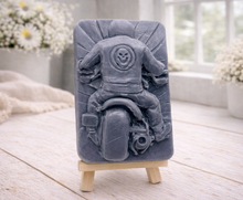 Load image into Gallery viewer, detailed handmade vegan soap gift featuring a motorcycle rider with a skull emblem on their jacket, displayed on a wooden easel against a whimsical farmhouse decor background