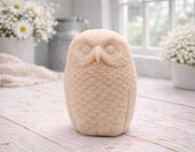 Load image into Gallery viewer, A detailed handmade vegan soap in the shape of an owl with intricate feather textures, displayed on a light wooden table with white flowers in the background.