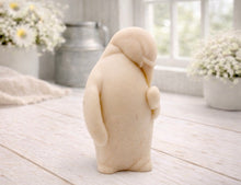 Load image into Gallery viewer, A 3D handmade vegan soap sculpted as a standing penguin tenderly cradling a heart against its chest, displayed on a light wooden surface in a bright farmhouse setting.