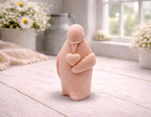 Load image into Gallery viewer, A 3D handmade vegan soap sculpted as a standing penguin tenderly cradling a heart against its chest, displayed on a light wooden surface in a bright farmhouse setting.
