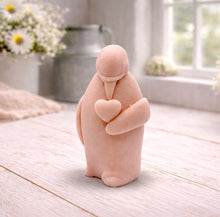Load image into Gallery viewer, A handmade vegan soap sculpted as a standing penguin tenderly cradling a heart against its chest, displayed on a light wooden surface in a bright farmhouse setting.