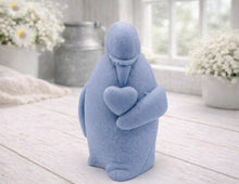 Load image into Gallery viewer, A 3D handmade vegan soap sculpted as a standing penguin tenderly cradling a heart against its chest, displayed on a light wooden surface in a bright farmhouse setting.