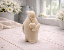 Load image into Gallery viewer, A 3D handmade vegan soap sculpted as a standing penguin tenderly cradling a heart against its chest, displayed on a light wooden surface in a bright farmhouse setting.
